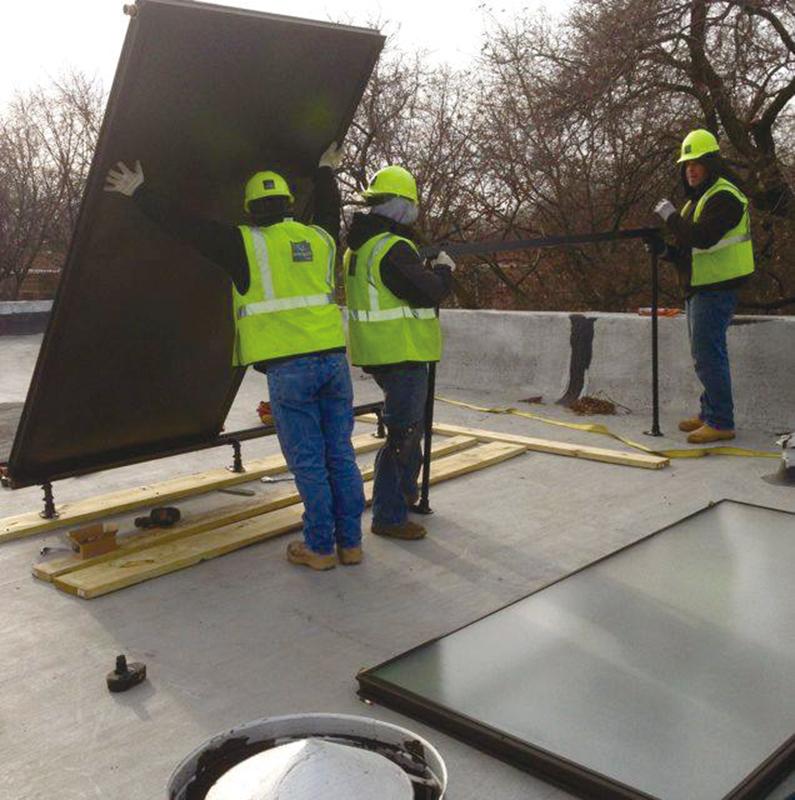 Workers install solar panels on the roof of a building. SHOP allows participants to purchase solar-powered hot water heaters as a group in order to reduce costs.