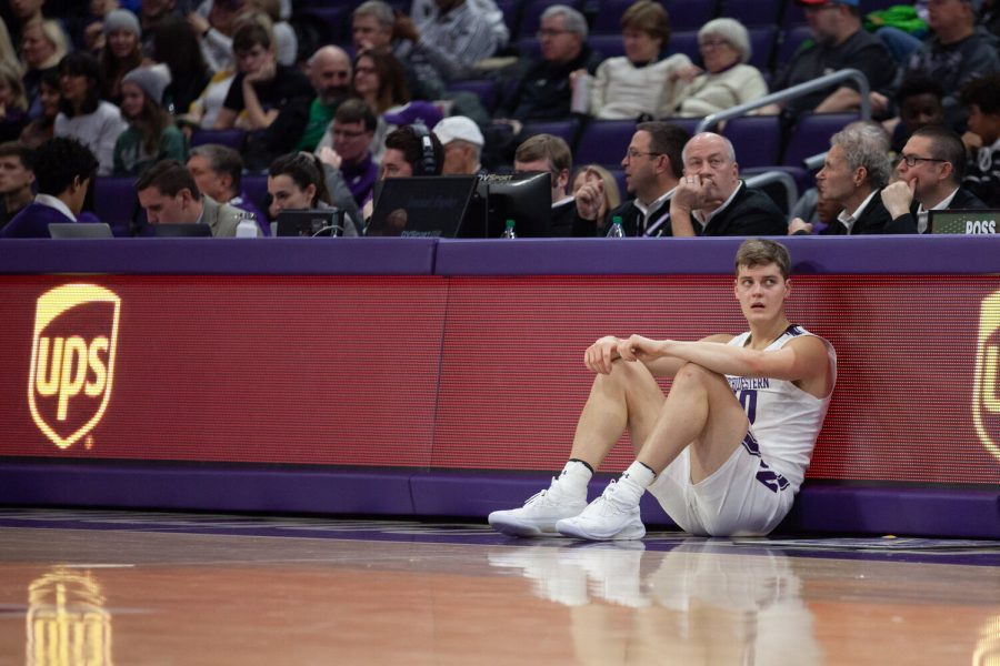 A Northwestern basketball player sits crouched in front of a red table