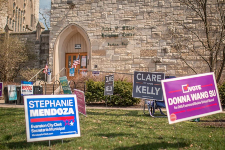 Brightly colored campaign signs dot the lawn of a tan brick building.