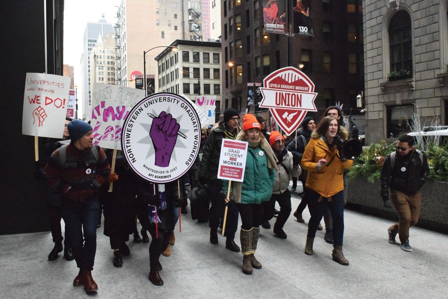 Graduate students hold up signs as they march at a protest.