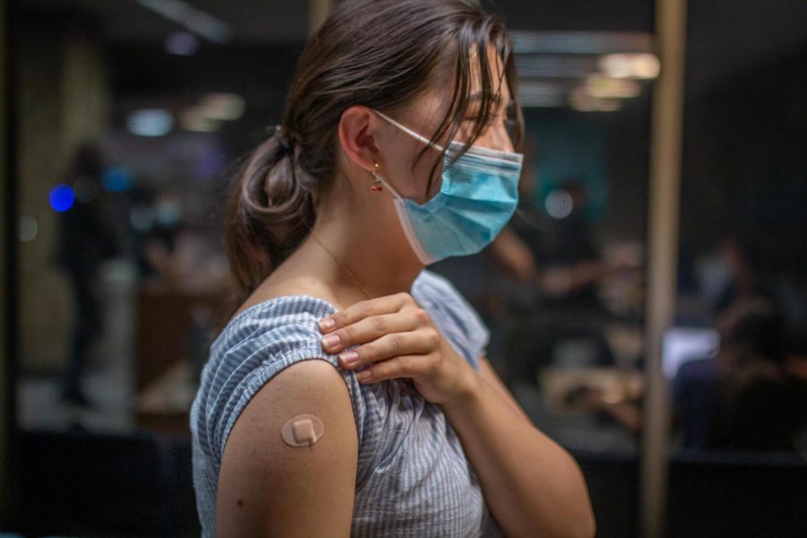 Freshman Courtney Sullivan Wu smiling, looking rightward, showing a bandaid on her arm. She is wearing a blue shirt and has a blue face mask on.