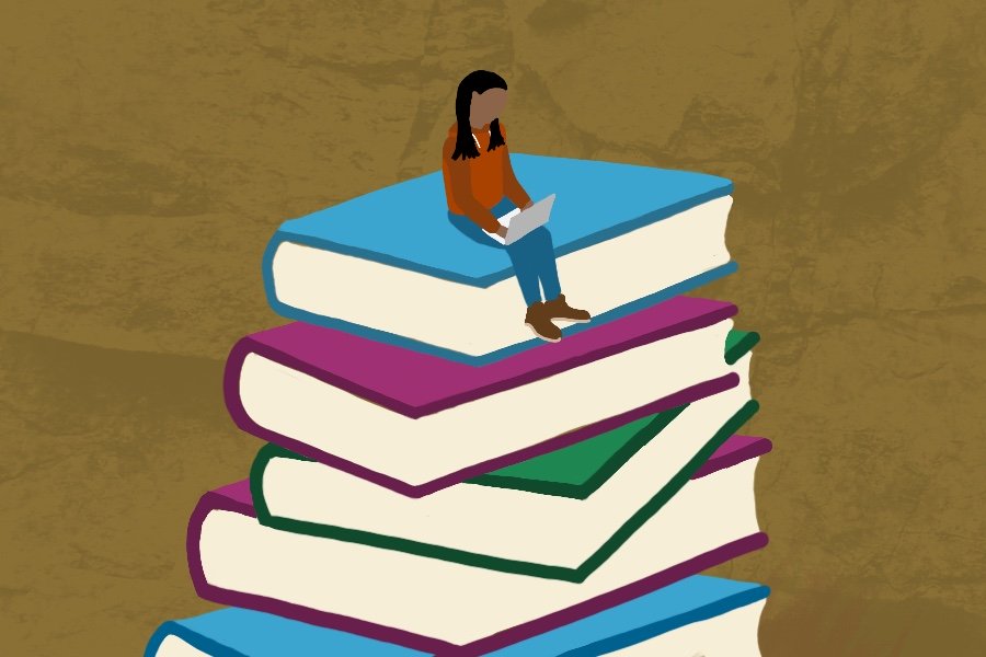 A young girl of color types on a computer while sitting on top of an oversized stack of books.