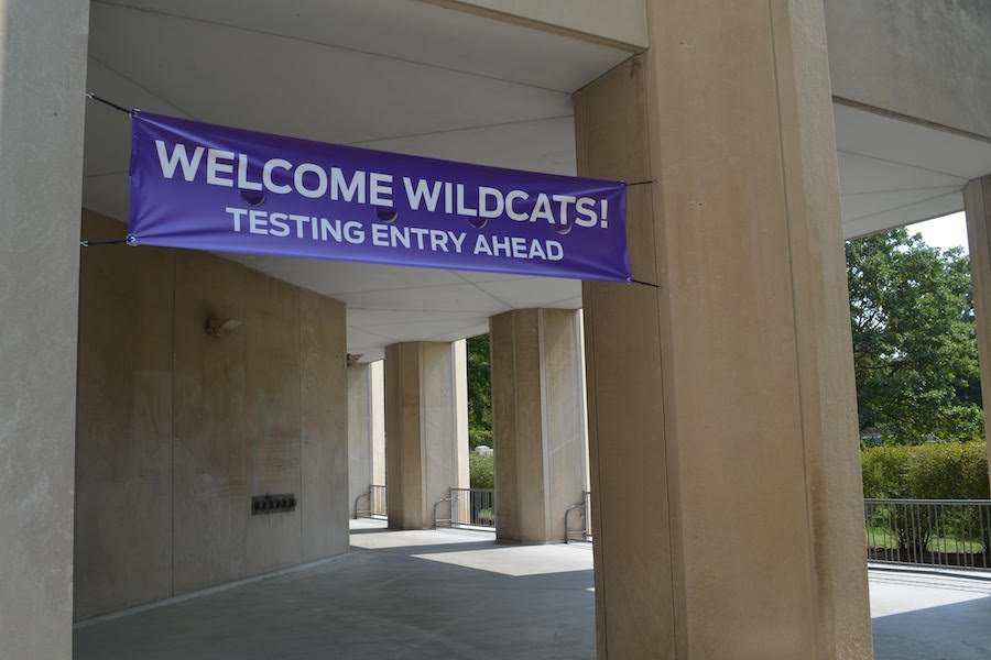 A gray and tan walkway with five visible pillars. A purple banner reads “Welcome Wildcats! Testing Entry Ahead.”