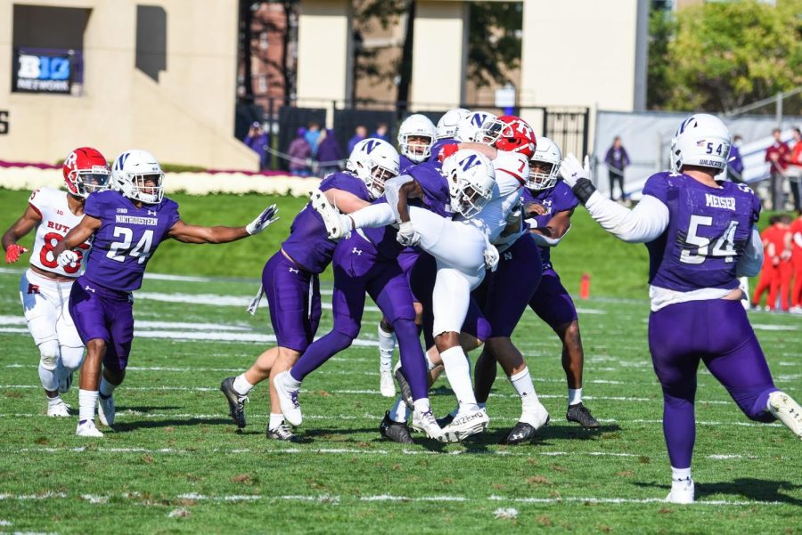 A group of players in purple football jerseys surround and tackle a player in a red jersey.