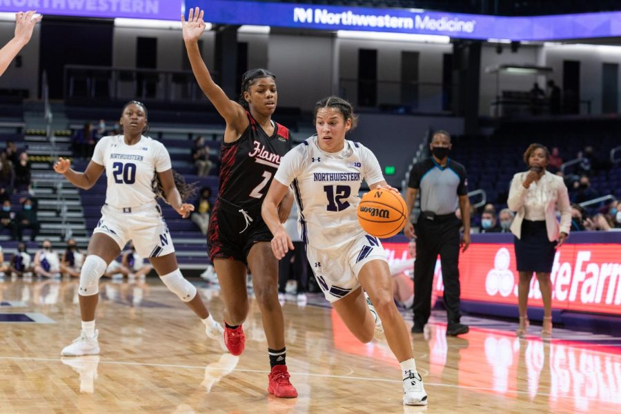A basketball player wearing a purple-and-white Northwestern jersey and shorts with the number ‘12’ on it drives down a basketball court dribbling a basketball.