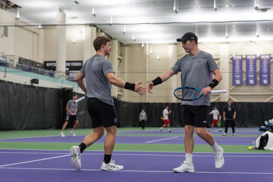 Male tennis player in black hat, gray shirt and black shorts stops running on a purple and green court.