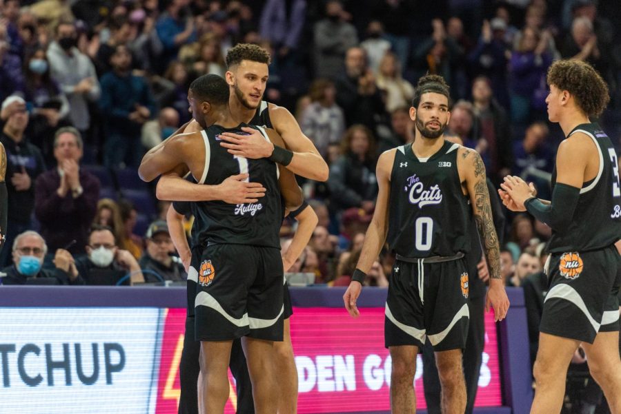 Two basketball players in black jerseys and black uniforms hug.