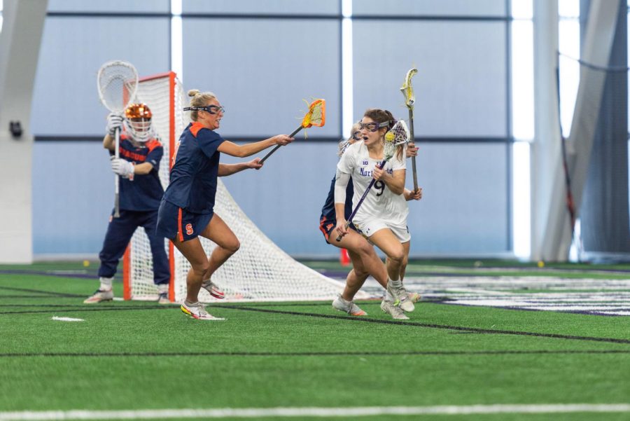 Lacross players hold sticks near goal.