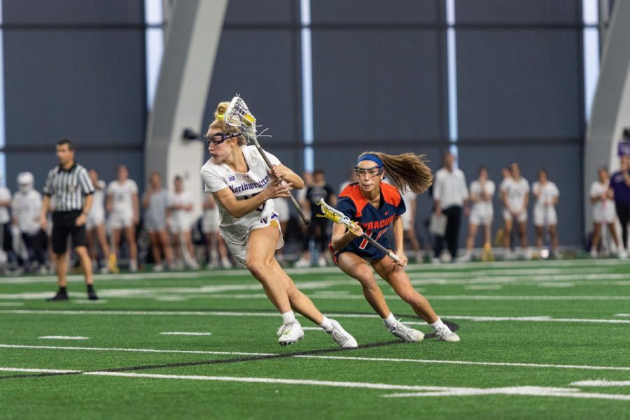 A woman in a white jersey runs away from another player in a blue jersey. The woman in the white jersey has the ball.