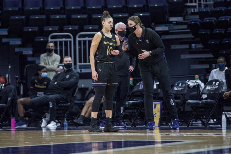 Masked coach dressed in black instructs player in white jersey