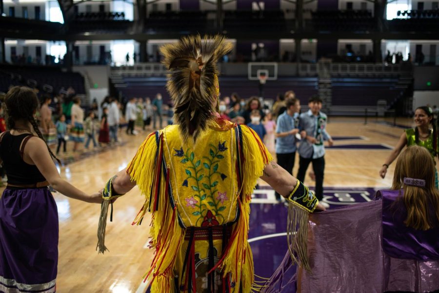 A group of people link arms on a basketball court. The closest person wears yellow regalia.