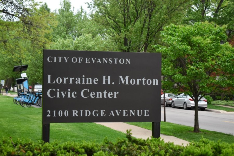 Gray sign with white lettering and green trees in the background.
