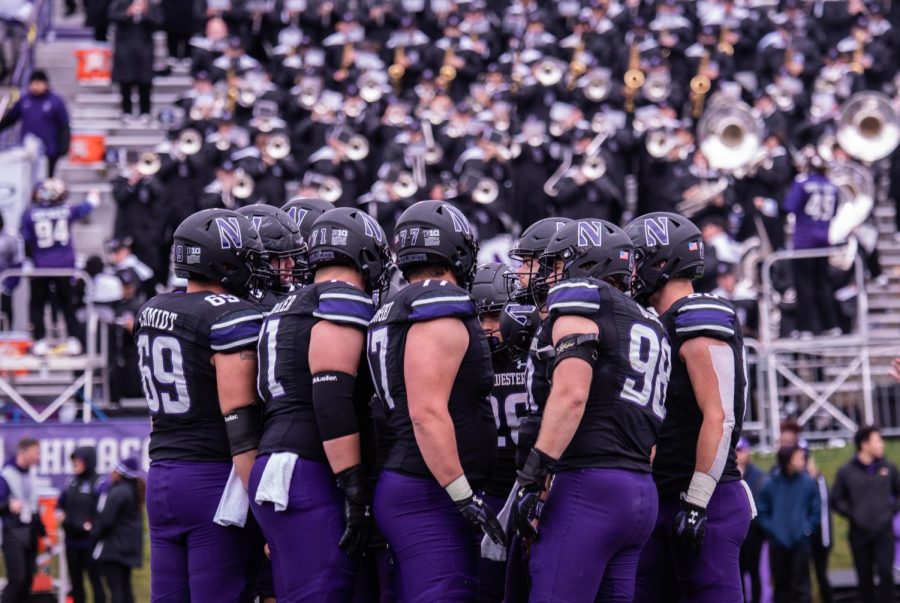 Football players in black helmets and black jerseys huddle together.