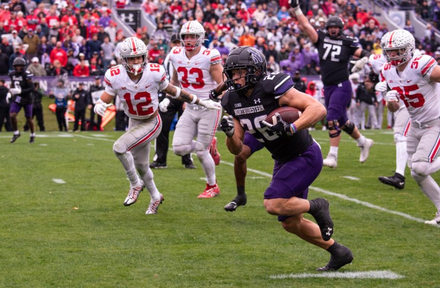 Player in black uniform sprints past a defender in a white uniform on a football field.