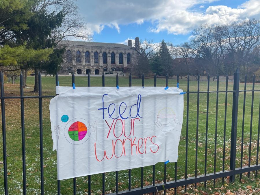 A paper banner with the words “Feed your workers” and illustrations of food on a fence in front of a green meadow.