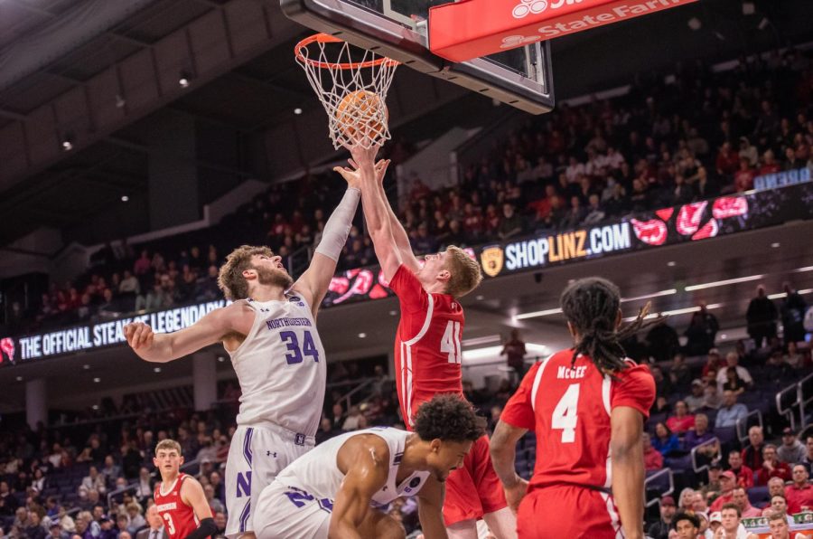 Two basketball players reach up for the basketball as it falls through the net.