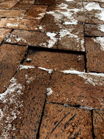 A brick is depressed on a sidewalk coated in snow.