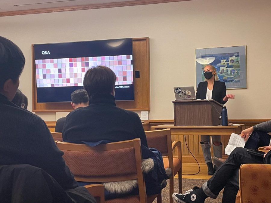 A professor talks in front of a slideshow presentation to an audience.