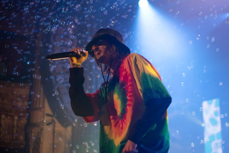 A singer surrounded by bubbles on stage sings into a microphone.