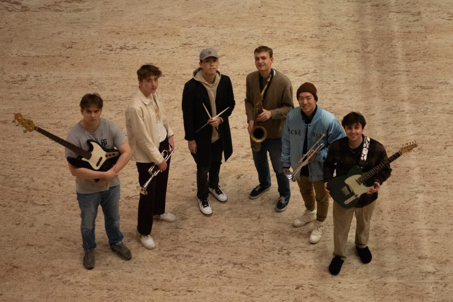 Photo looks down on the six members of Muse etc. standing in a line holding their respective instruments.
