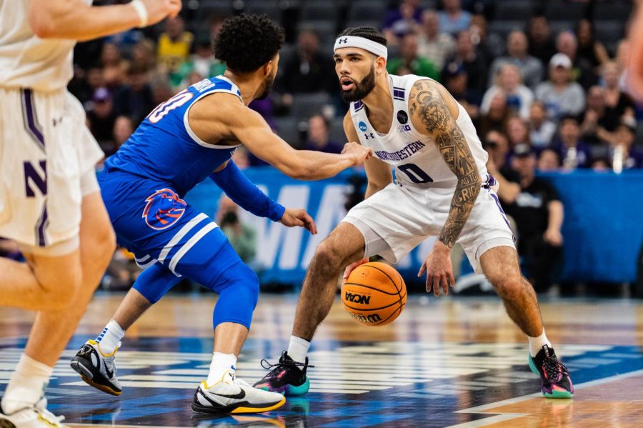 A basketball player in a white NU jersey dribbles the ball while staring down a defender in a blue Boise State jersey.