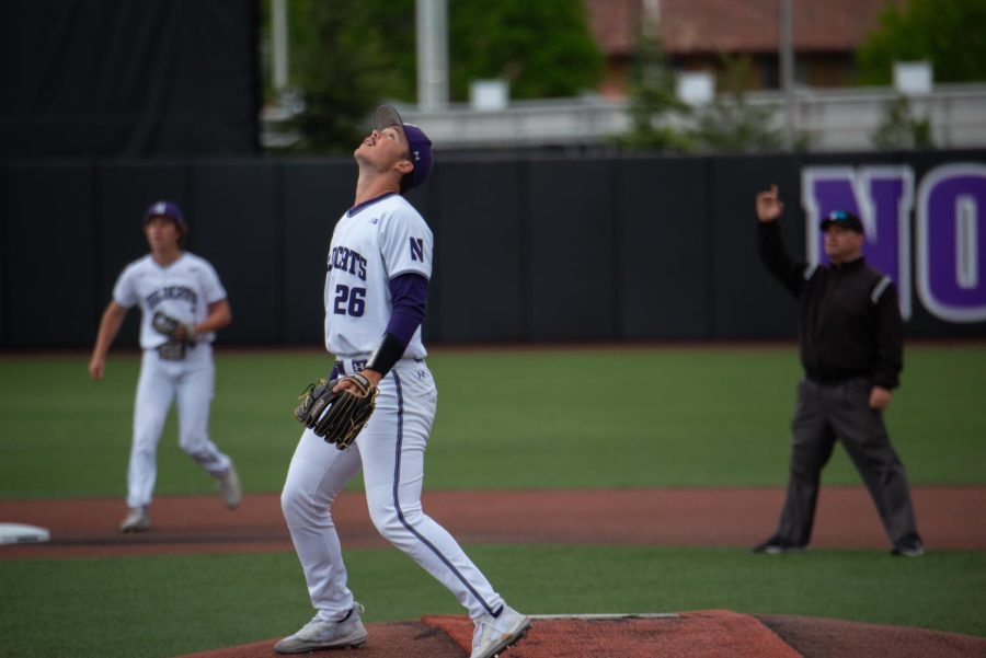 A baseball player in a white uniform stares upward.