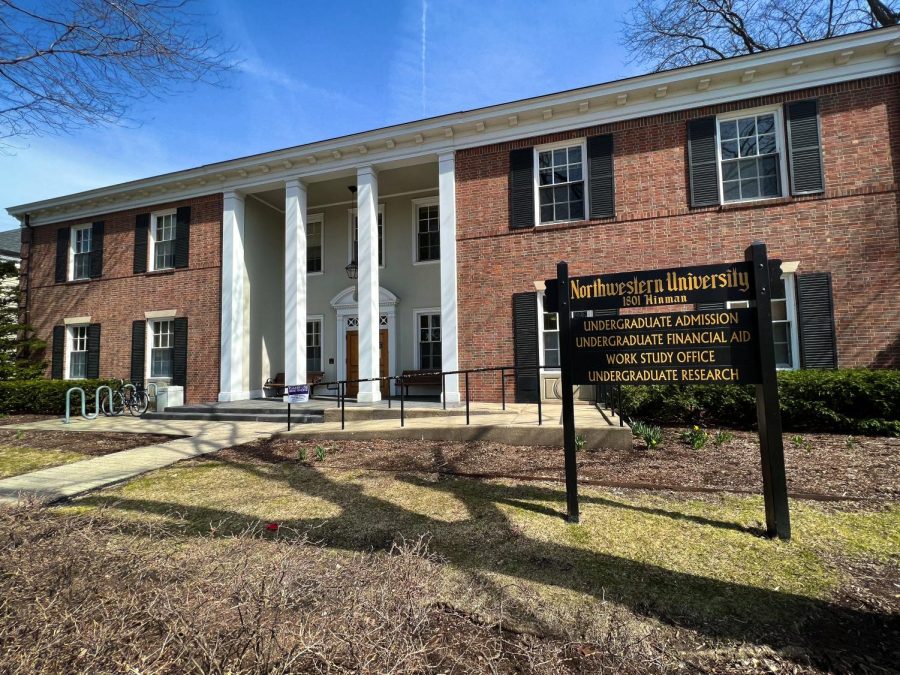 A brick building with windows and white pillars in the front. A black sign reads “Northwestern University” and identifies the several offices that work in the building.