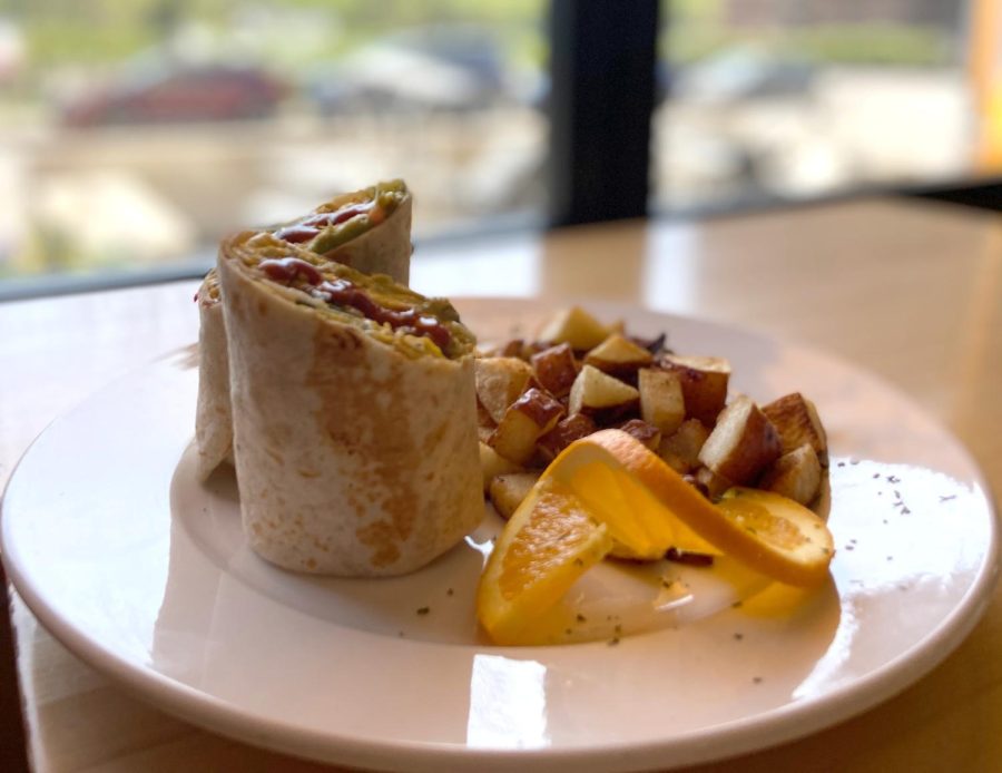 A breakfast burrito sits on a table in front of a window.