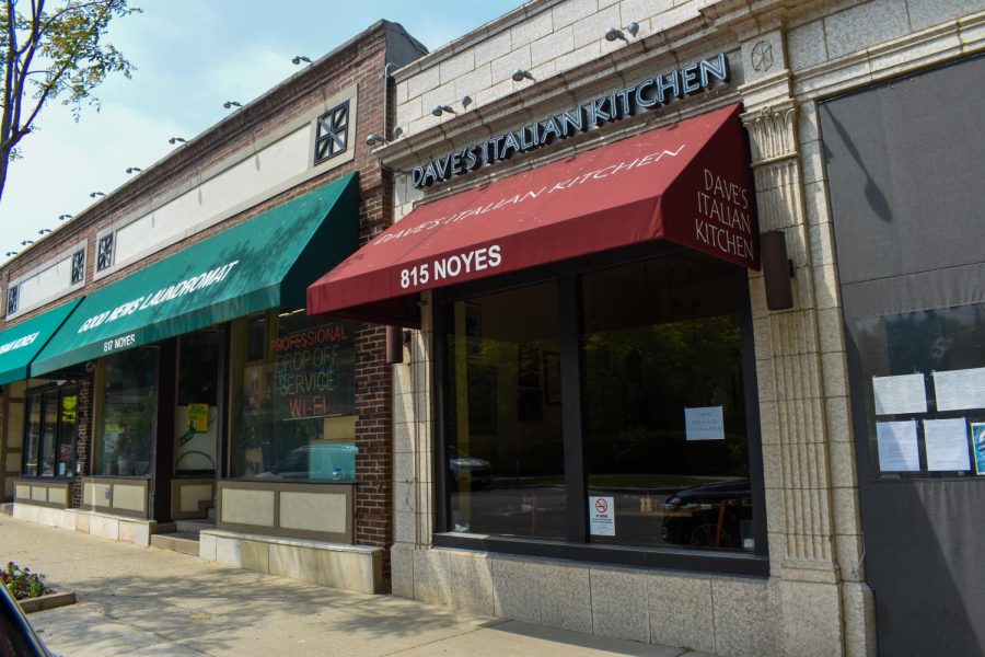 A tan building with a red awning. A sign above reads “Dave’s Italian Kitchen.” To the left are brick buildings.