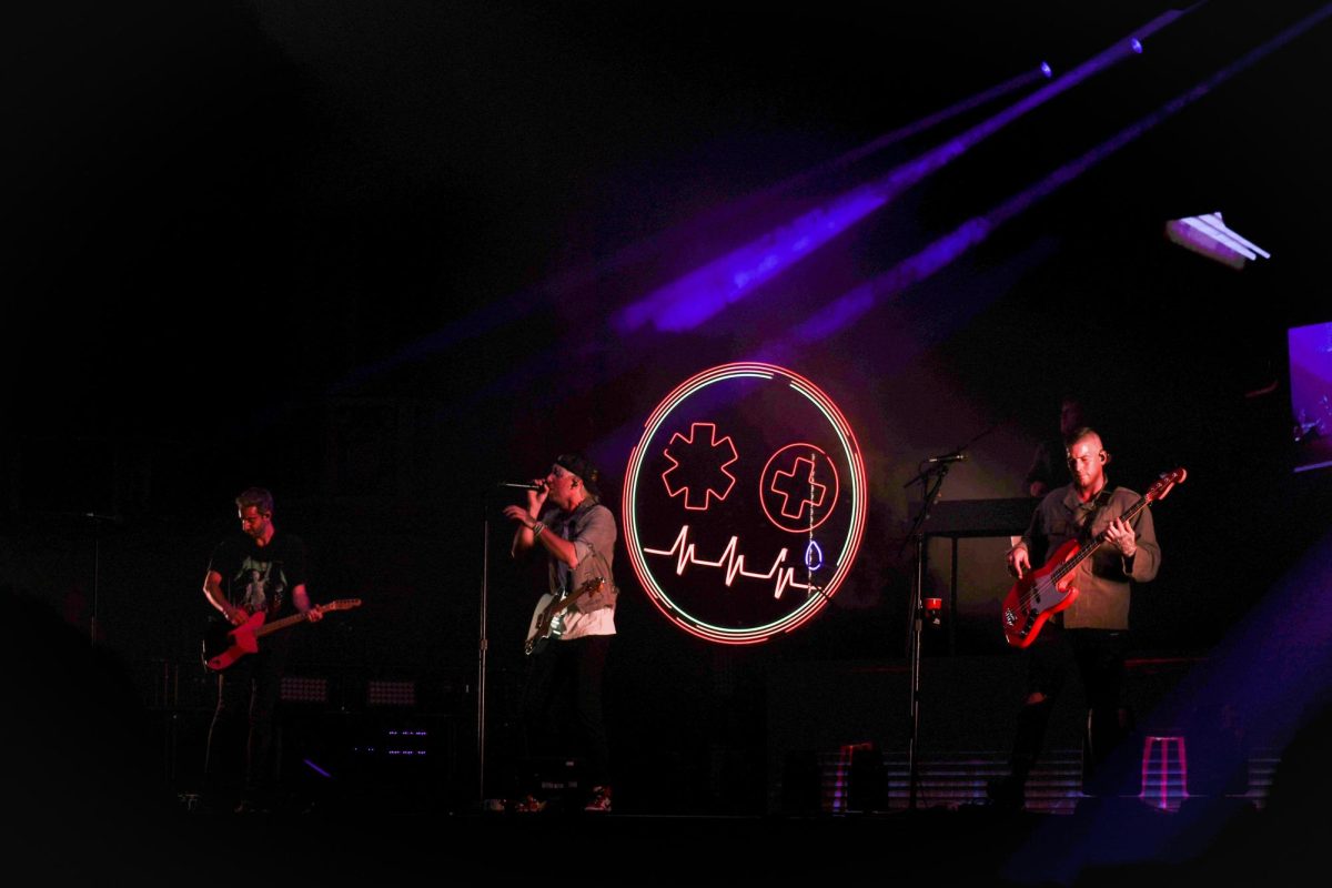 Three men holding guitars play music, with the man in the middle singing into a microphone.