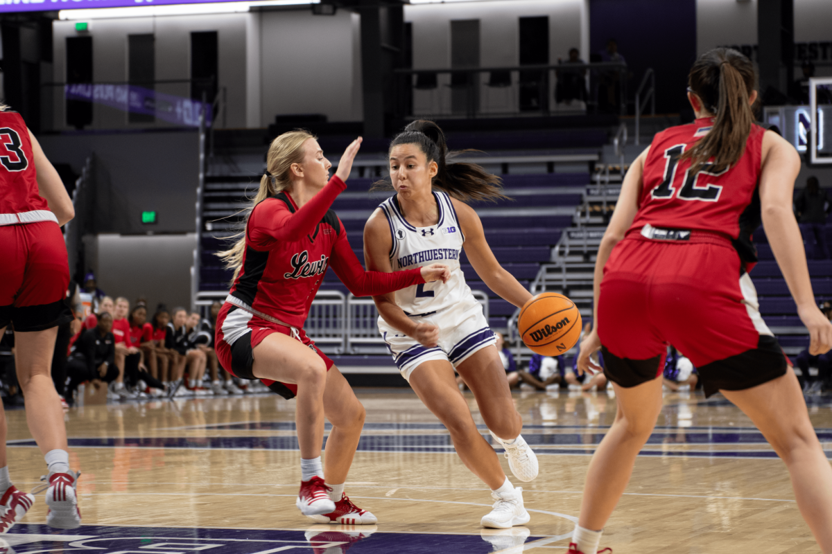 An athlete in a white jersey dribbles a basketball around a defender in a red jersey.