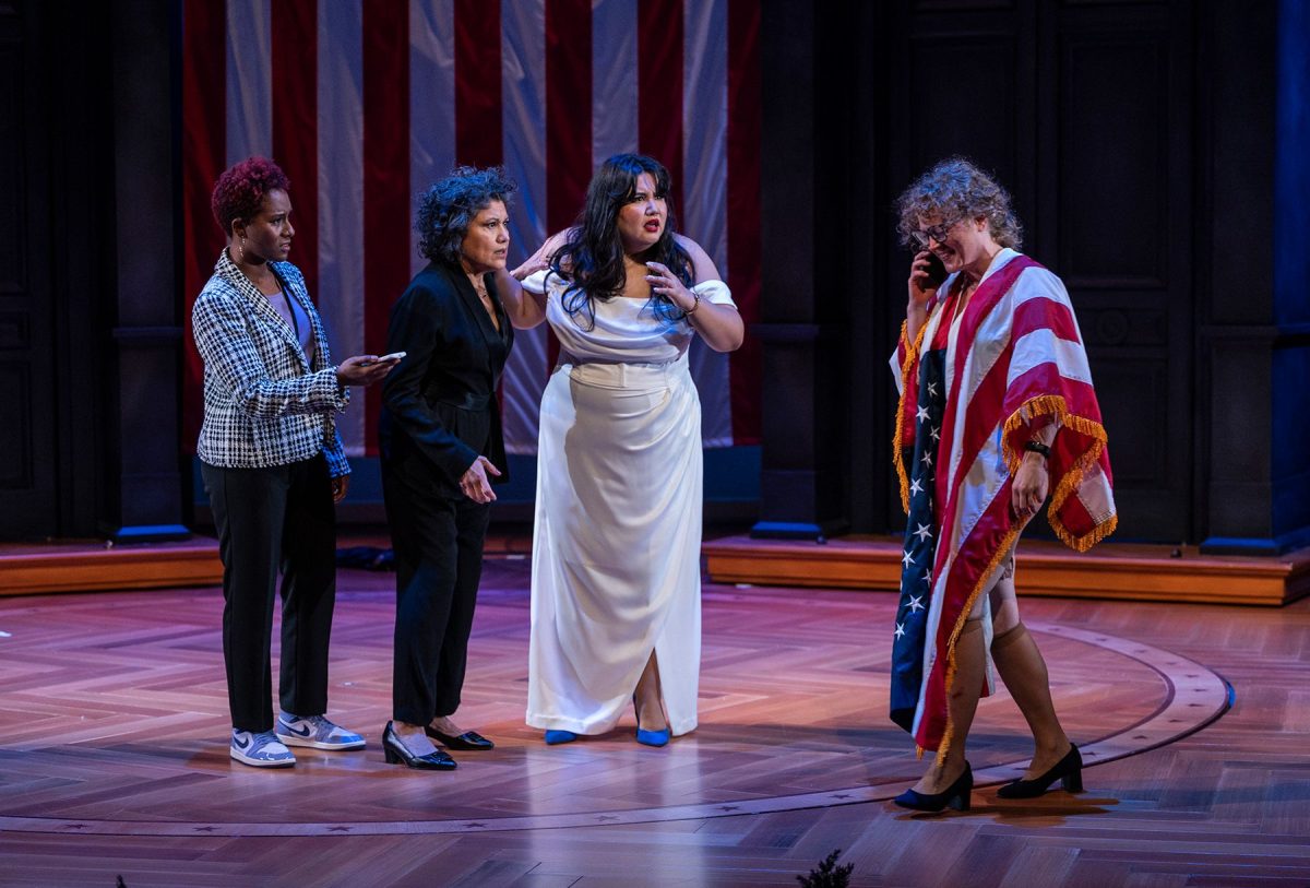 Three women confusedly watching a woman draped in an American flag as she talks on a cell phone.