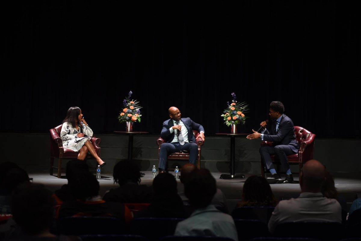 Three people sit in chairs on a stage holding microphones and talking to each other.
