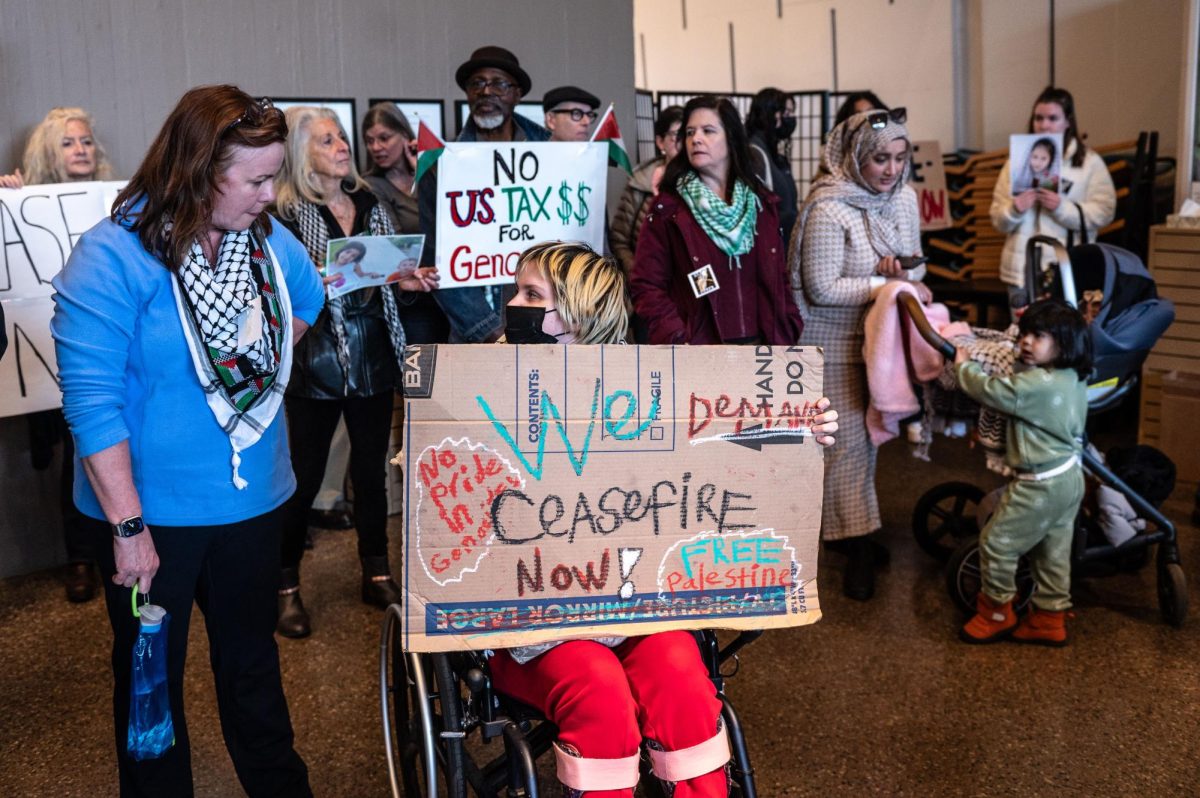 People look at one another while holding a sign that reads “We demand ceasefire now.”