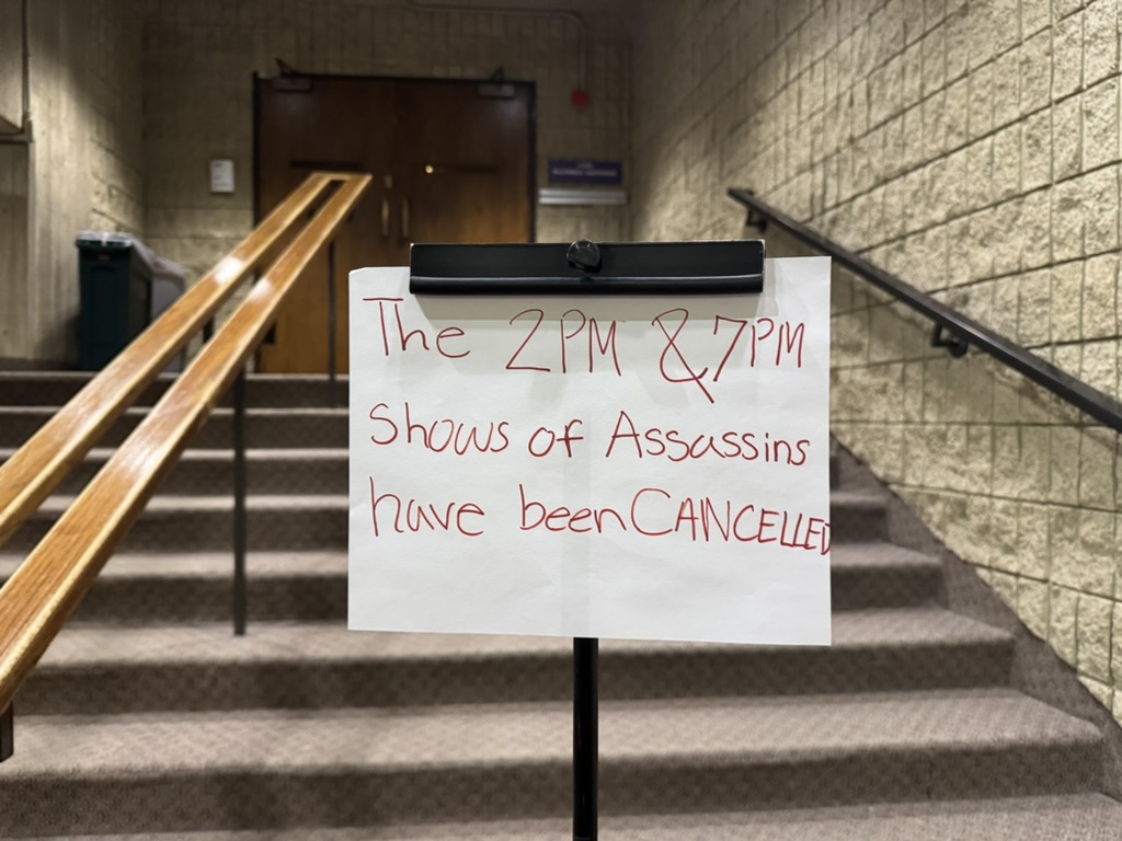 A sign reading, “The 2 p.m. and 7 p.m. shows of ‘Assassins’ have been canceled,” stands in front of an auditorium’s closed doors.
