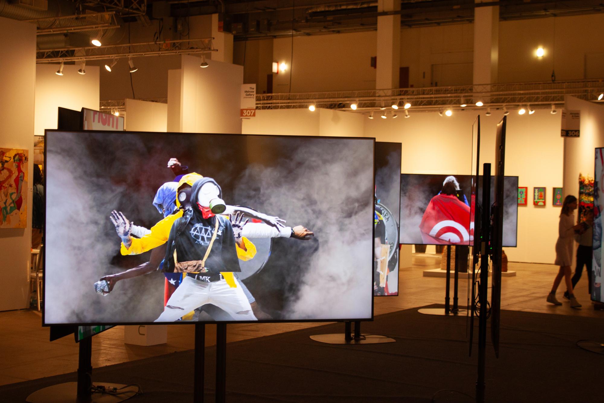 A multimedia presentation where multiple TV screens showcase people wearing gas masks. On each screen, the people are also surrounded by smoke.