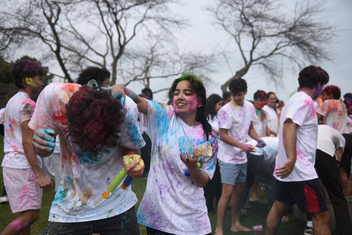 A person covered in paint and powder smears blue powder onto the clothes of another person.