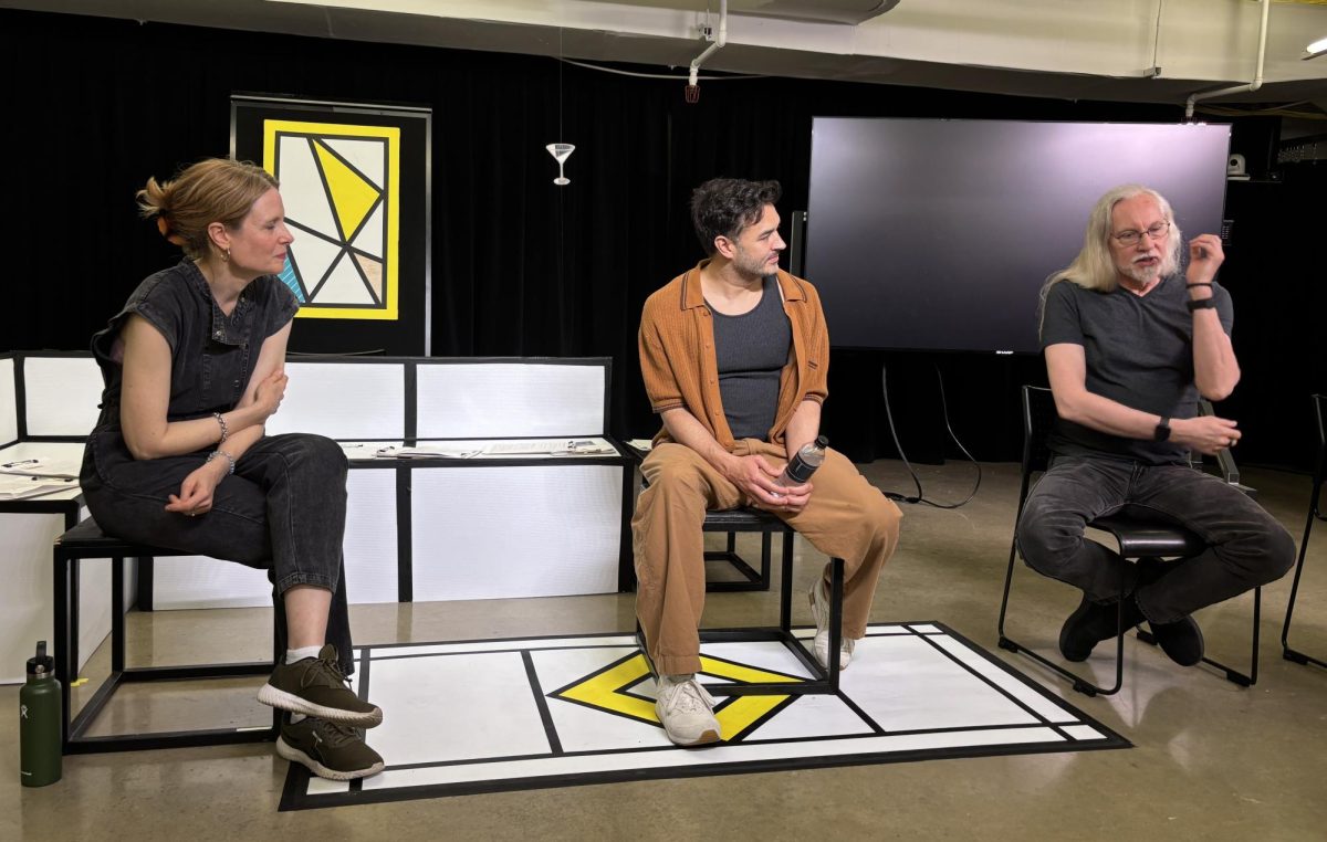 Three people sit in black chairs in front of a white couch, television, yellow painting and hanging martini glass.