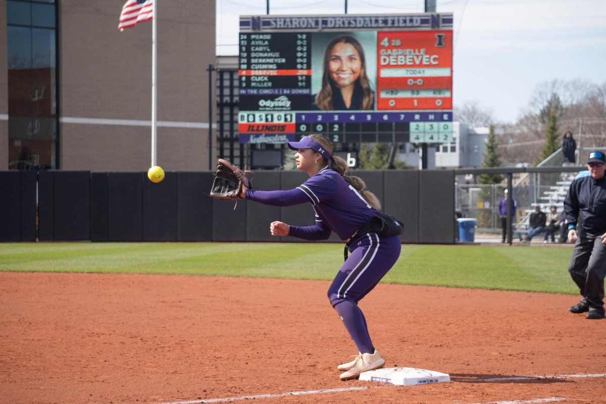 A player catches a softball as she stands on a base.