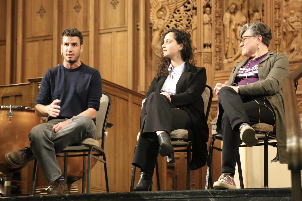 Three people sit in chairs on a stage
