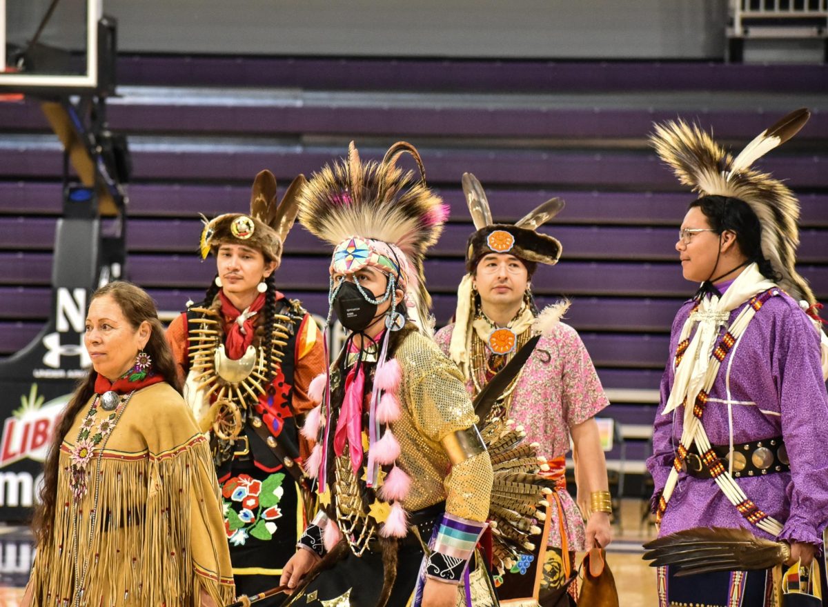 A group of Native American dancers steps into the arena in full regalia.