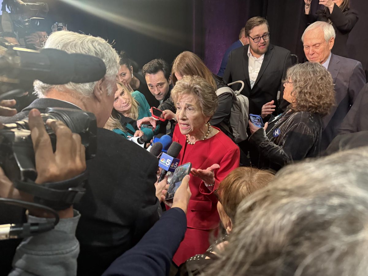 A woman surrounded by people speaks into a microphone.