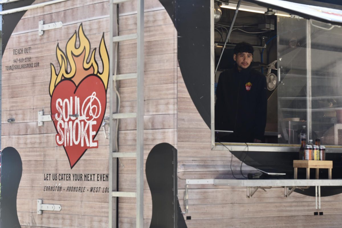 A person in a black zip-up stands inside a wooden food truck belonging to Soul & Smoke.