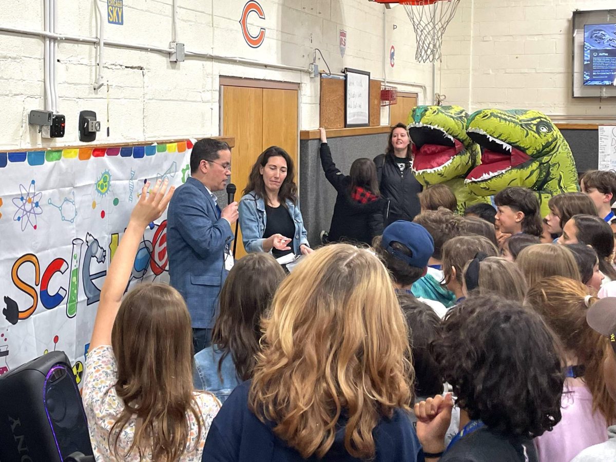 A crowd of kids gather around two people while one speaks into a microphone.