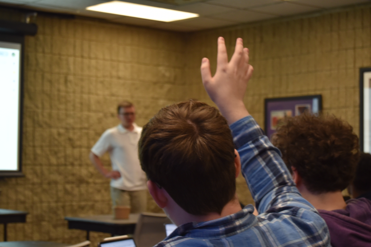 A man wearing a flannel raises his hand.