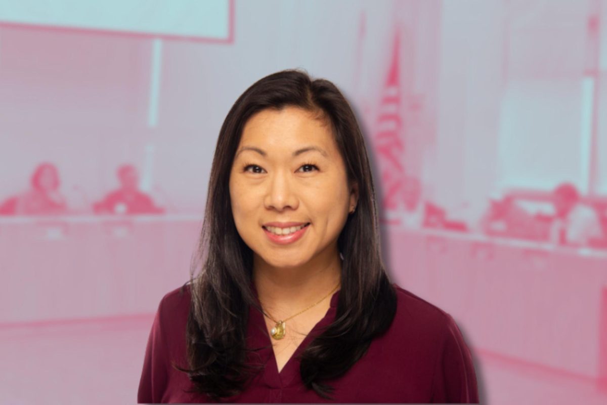 A woman in front of a pink background of people sitting at tables.