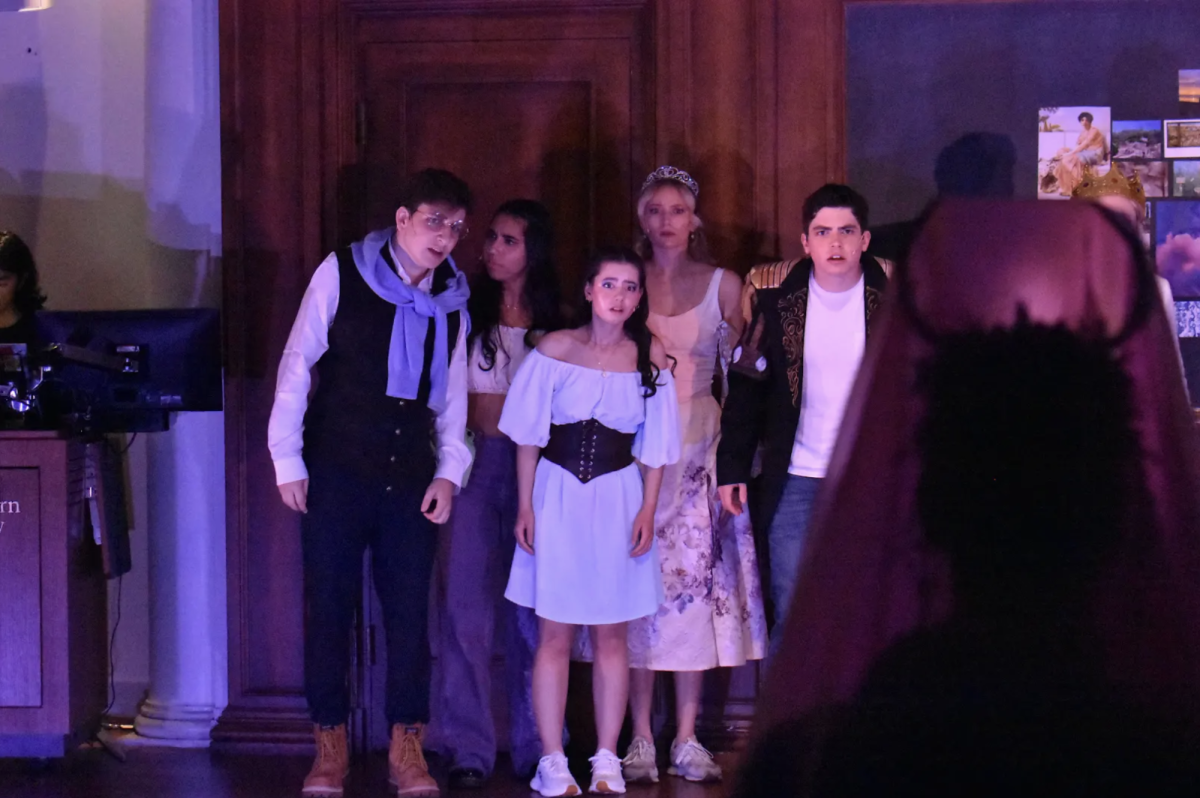 A group of people stand on stage staring at a person in an antler headpiece offstage.