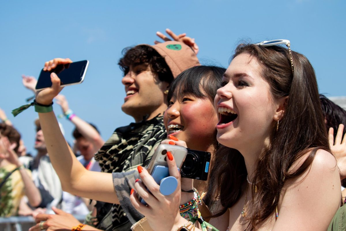 Three students cheer in front of a blue sky.