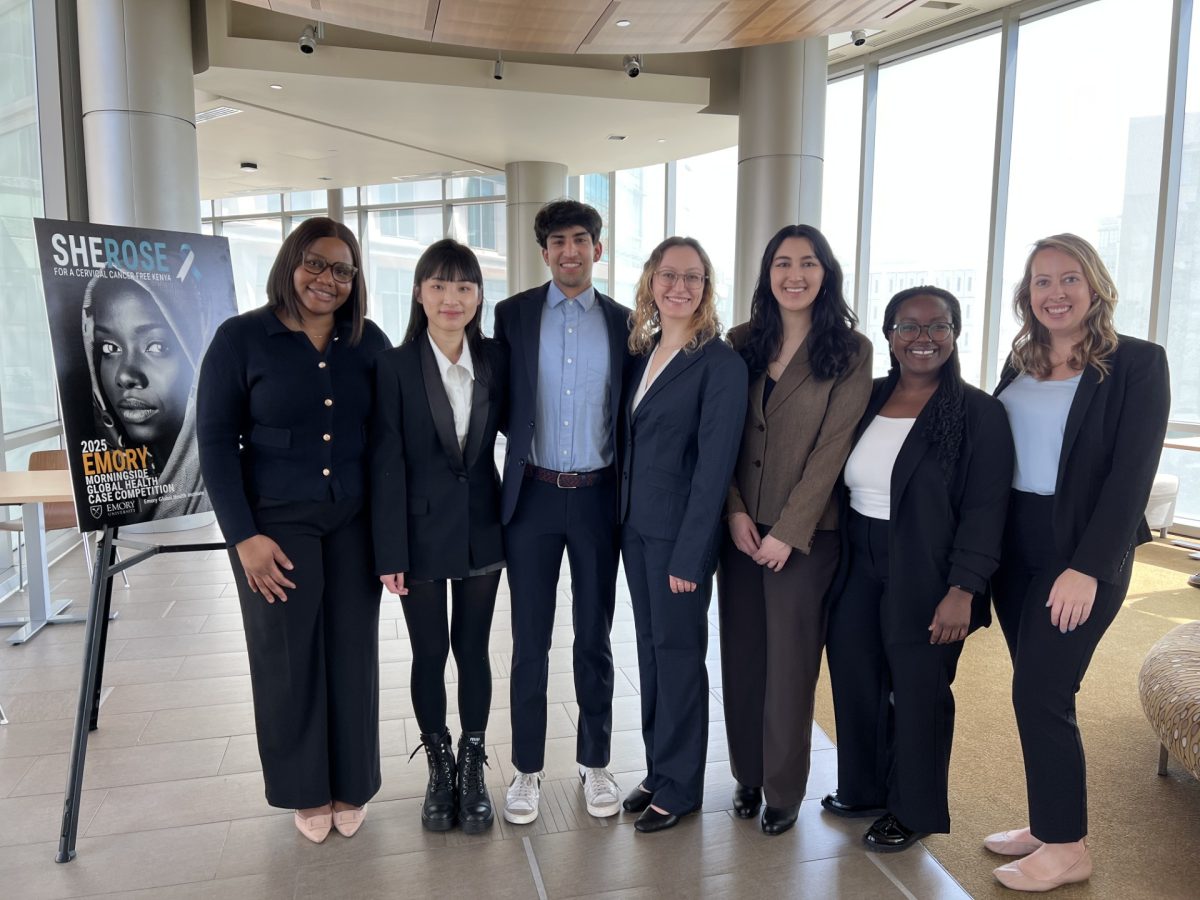 Six Feinberg students and one professor pose next to a sign promoting the 2025 Emory Morningside Global Health Case Competition.