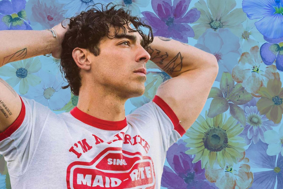 Joe Jonas poses with his hands on his head in front of a flower pattern